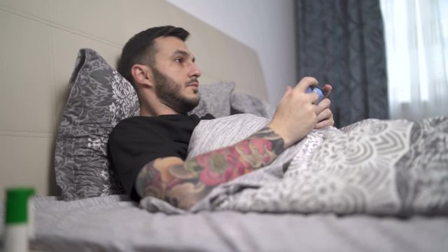 Man in home quarantine playing video games lying in bed