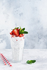 Fresh healthy milkshake yogurt with chia seeds and strawberries in a glass beaker against a gray concrete background. Selective focus