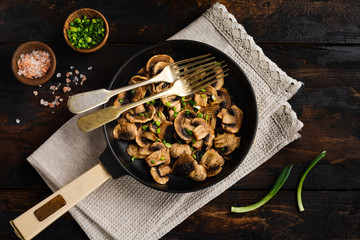 Fried Champignon mushrooms in a cast-iron old pan on an old dark wooden rustic background for frying. Top view.