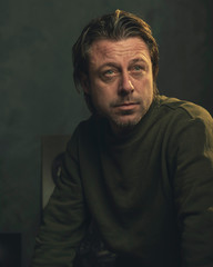 Middle aged man with stubble beard in green sweater.