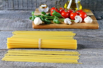 Uncooked spaghetti next to the fresh tomatoes and mushrooms on the grey wooden background.