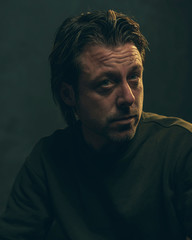 Middle aged man with stubble beard in green sweater.