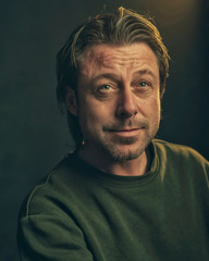 Middle aged man with stubble beard in green sweater.