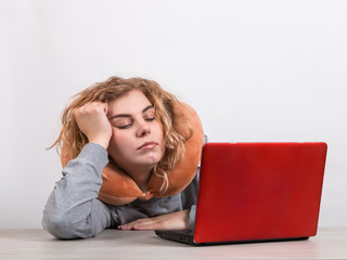 The girl works at the computer with pillow around her neck, on a white background. The concept of working from home, a sleepy lazy worker.