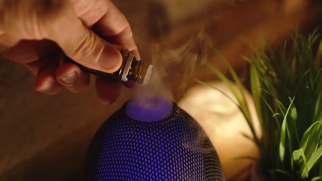 4k, Woman adding essential oil to electric diffuser lamp, candles on wooden table in room. Aromatherapy.