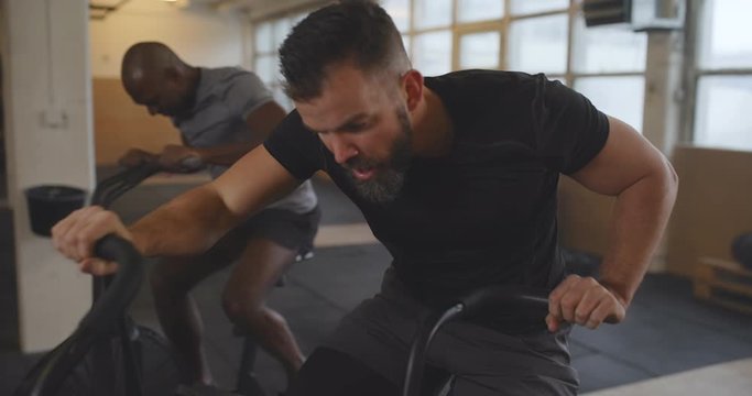 Two fit young men in sportswear finishing a cardio
workout on stationary bikes together at the gym