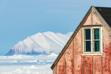 Fototapeta na wymiar Red house in front of mountains and frozen sea, Greenland.