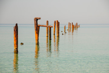 Seascape with blue calm water and rows of Rusty pipes with green algae on summer day. Rusty pipes remaining from old pier. Perspective leading to horizon, no people. Calm water.