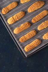 Homemade Savoyardi cookies on a baking sheet on a blue background. Top view, flat lay.