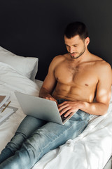handsome and shirtless freelancer using laptop in bedroom
