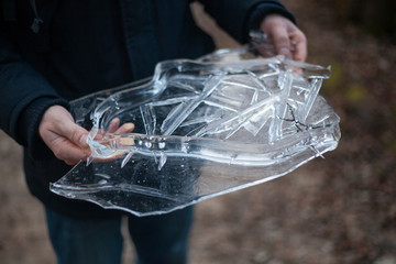 Ice in the hands. Cold spring background. A fragment of frozen water. The guy holds a glass piece of water in his hands.