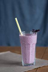 Blackcurrant milk smoothie with purple Basil and yellow straw on a textile tissue