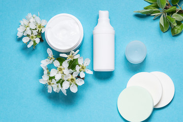Obraz na płótnie Canvas Fresh organic moisturizing cream, lotion and cosmetic sponges on light blue background with beautiful spring blossom twigs. Skin care concept.