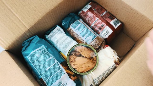 A man collects a food box for a donation to the poor during the Coronavirus pandemic. Various products in a box: cereals, butter, canned food in jars. Collection and delivery of grocery cartons.