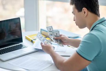 Dark-haired male sitting at his desk, calculating money