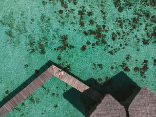 Aerial view of  couple lying on wooden pier in tropical resort with aqua mint ocean. Couple on wooden brown jetty on calm relaxing, top view