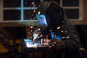 Focused welder designer wearing a helmet and wokring on a project by welding pieces of metal while...