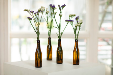 purple and white flowers in a brown beer bottle on a white table and a blurry background fathersday
