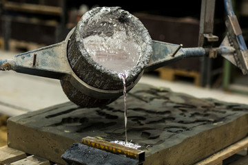 Metal sand casting technique pouring molten aluminum silver colored liquid into a mold in a...