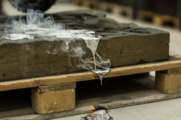 Metal sand casting technique pouring molten aluminum silver colored liquid into a mold while making...