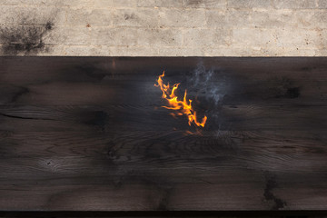 Detail of a burning big piece of oak wood, just burnt with a fire torch, creating flames and smoke,...