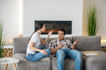 Brunette male and dark-haired female sitting on sofa, arguing about something
