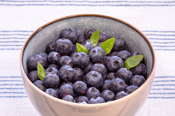 Close-up of a  bowl with blueberries inside with green leaf and on the kitchen table with tablecloth.
