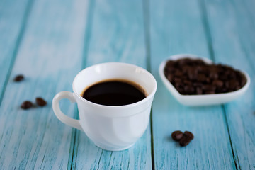 White cup with black coffee and coffee beans on an old blue wooden background.