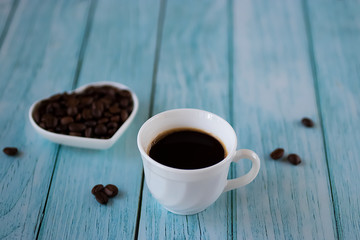 White cup with black coffee and coffee beans on an old blue wooden background.