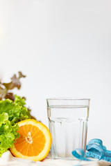 salade leaf. orange, cup of water and measuring blue tape on white background with copy space for text, healthy lifestyle and drinking water concept