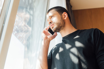 low angle view of man talking on smartphone near window at home