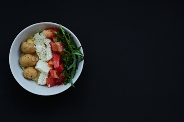 Black background and bowls with healthy, useful kus-kus breakfast with vegetables, tomatoes, mushrooms, arugula and cheese.