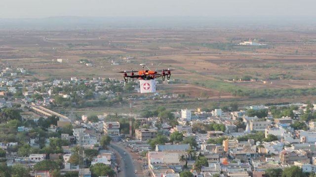 Aerial view of drone or quadcopter with Medical kit or Medicines moving above the town - Concept shipping medicines through drone during covid-19 or coronavirus Pandemic.