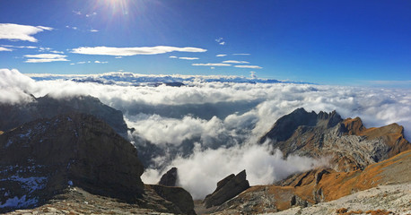 Cima de varias montañas entre las nubes bajas con el cielo azul de fondo