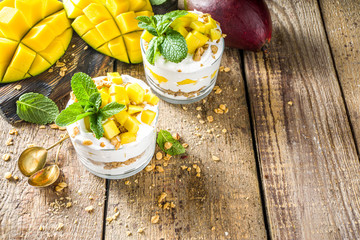 Summer breakfast layered dessert with mango and granola. Mango parfaits in portioned jars, rustic...