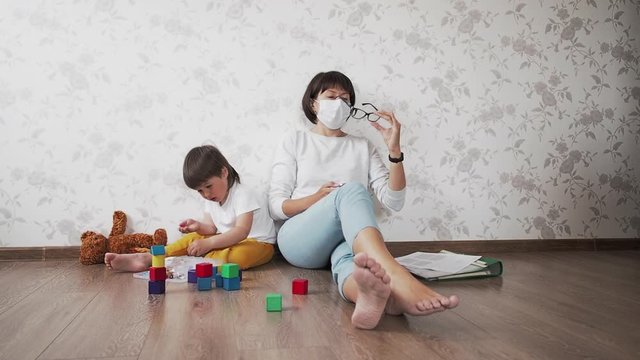 Mom and son sit at home quarantine because of coronavirus COVID19. Mother works remotely with laptop, son plays with toy blocks. Self isolation at home.