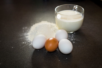 Ingredients for baking on a black background. Ingredients for the dough. Eggs, milk, flour.