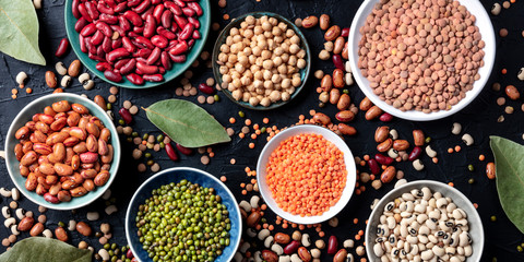 Legumes assortment panorama, overhead shot on a dark background. Lentils, soybeans, chickpeas, red...