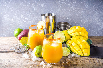 Summer tropic mexican cold cocktail. Mango margarita cocktail, with tequila, lime, lemon, hot chili jalapeno peppers. Wooden background with bar party utensils copy space