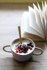 Bowl of rice porridge with berries and open book. Selective focus.