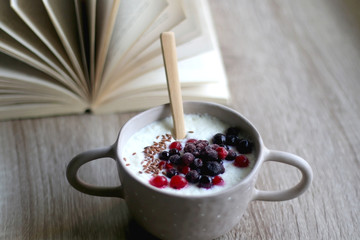 Bowl of rice porridge with berries and open book. Selective focus.