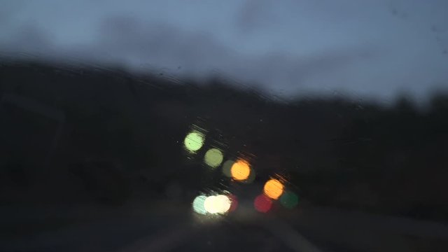 Parabrisas de un coche bajo una tormenta. Llueve y se reflejan las luces de los coches. Cámara lenta.