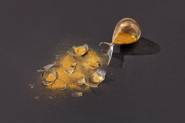 Crashed sandglass with golden sand on a black background.