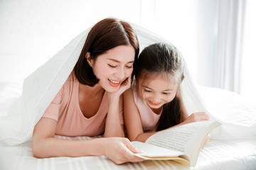 happy mother and  daughter child reading book together in bed