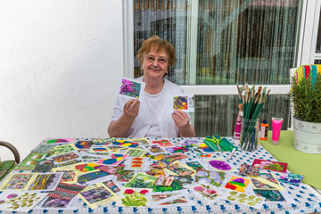 84 jährige ältere Frau zeigt lächelnd ihre Bilder, Malen im Garten während der Quarantäne,...