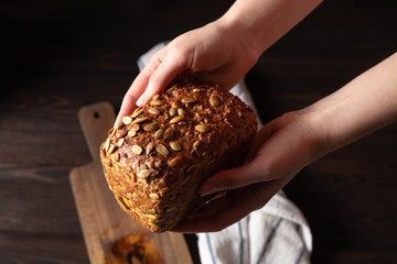 Baker holding fresh loaf of bread with pumpkin seeds in the hands