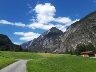 Weg der Via Claudia führt über eine Wiesenlandschaft hin zu den Bergen der Alpen