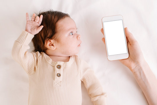 Baby newborn on white bed, woman holding mobile phone in hand