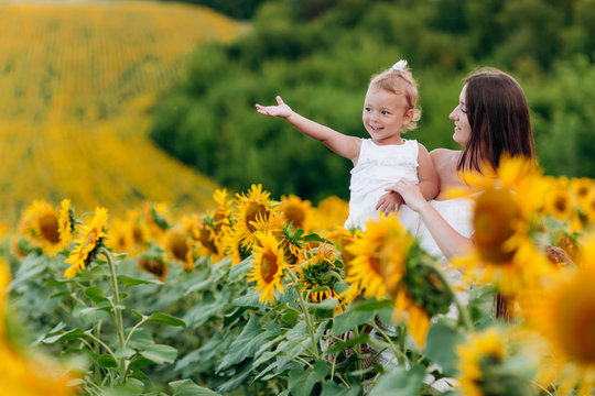 Happy mother with the daughter in the field with sunflowers. mom and baby girl having fun outdoors. family concept. mother's, baby's day. summer holiday