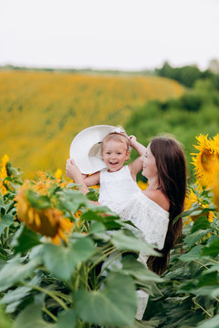 Happy mother with the little daughter in the field of sunflowers. mom and baby girl in mom's hat having fun outdoors. family concept. mother's, baby's day. summer holiday